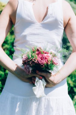 Gelin elinde güllerden bir buket tutuyor, düğün çiçekleri. Güzel bohem düğün çiçeği buketi. Bir buket gülü elbisesi olan kız..