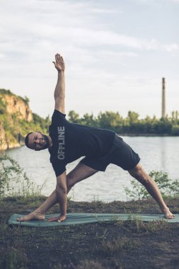 Sportif sakallı adam kayalık deniz kıyısında kol dengesi kuruyor. Taş ocağı gölünde Uluslararası Yoga Günü.