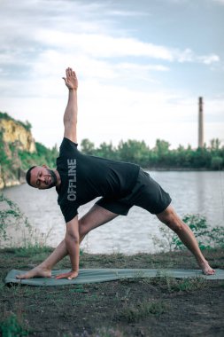 Sportif sakallı adam kayalık deniz kıyısında kol dengesi kuruyor. Taş ocağı gölünde Uluslararası Yoga Günü.