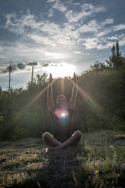 Mükemmel vücut adamının silueti günbatımı arka planında kayanın üzerinde yoga yapıyor. Uluslararası Yoga Günü.