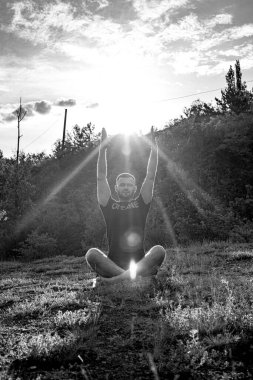 Mükemmel vücut adamının silueti günbatımı arka planında kayanın üzerinde yoga yapıyor. Uluslararası Yoga Günü.