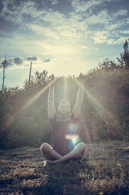 Mükemmel vücut adamının silueti günbatımı arka planında kayanın üzerinde yoga yapıyor. Uluslararası Yoga Günü.