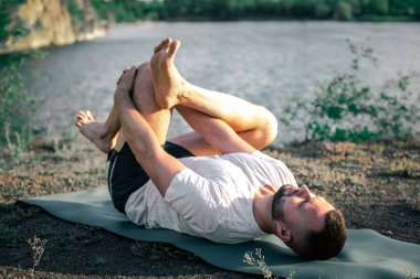 Genç sakallı adam yoga yapıyor ve Asana 'da duruyor. Güzel dağ taş ocağı gölü manzarası. Karmaşık ve komik yoga filmi. Uluslararası Yoga Günü