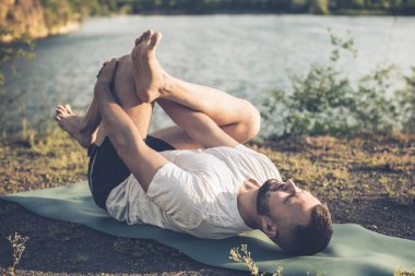 Sabah parkında yoga yapan genç bir adam. Sakallı adam rahatla ve doğada esne. Uluslararası Yoga Günü