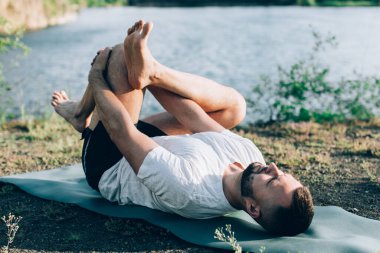 Sabah parkında yoga yapan genç bir adam. Sakallı adam rahatla ve doğada esne. Uluslararası Yoga Günü