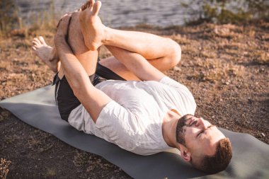 Sabah parkında yoga yapan genç bir adam. Sakallı adam rahatla ve doğada esne. Uluslararası Yoga Günü