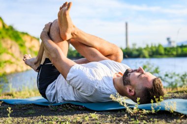 Sabah parkında yoga yapan genç bir adam. Sakallı adam rahatla ve doğada esne. Uluslararası Yoga Günü