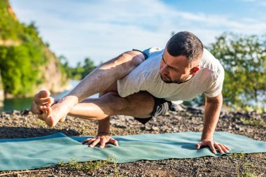 Sabah ve akşam yakışıklı genç bir adam yazın açık havada taş ocağı gölünün kıyısında yoga egzersizi yapıyor. Sağlıklı aktif yaşam tarzı kavramı.