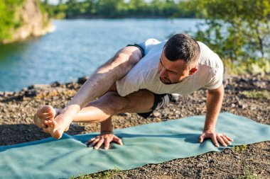 Sabah ve akşam yakışıklı genç bir adam yazın açık havada taş ocağı gölünün kıyısında yoga egzersizi yapıyor. Sağlıklı aktif yaşam tarzı kavramı.