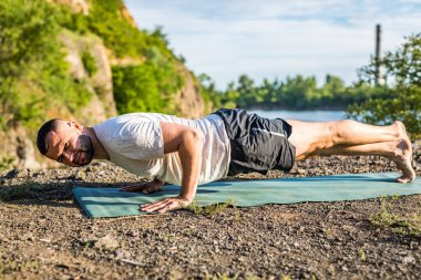 Sabah ve akşam yakışıklı genç bir adam yazın açık havada taş ocağı gölünün kıyısında yoga egzersizi yapıyor. Sağlıklı aktif yaşam tarzı kavramı.