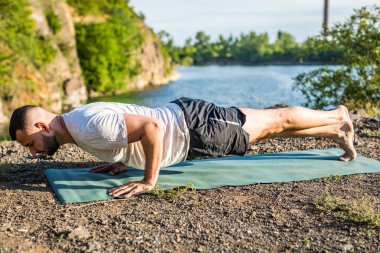 Sabah ve akşam yakışıklı genç bir adam yazın açık havada taş ocağı gölünün kıyısında yoga egzersizi yapıyor. Sağlıklı aktif yaşam tarzı kavramı.