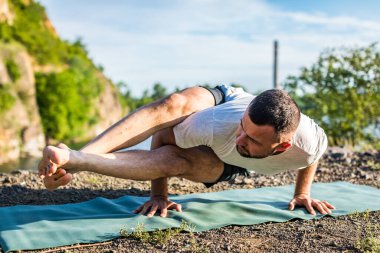 Sabah ve akşam yakışıklı genç bir adam yazın açık havada taş ocağı gölünün kıyısında yoga egzersizi yapıyor. Sağlıklı aktif yaşam tarzı kavramı.
