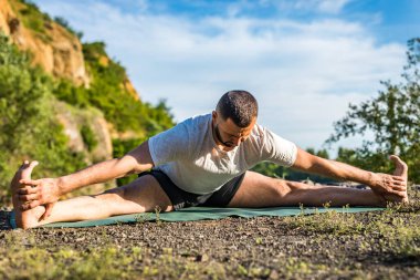 Genç fitness adamı taş ocağı gölünde yoga egzersizi yapıyor. Sakallı yakışıklı genç adam yoga egzersizi yapıyor..