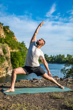Elleri ve bacakları eşe uzatan bir adam. Sakallı adam taş ocağında ve dağlarda yoga yapıyor..