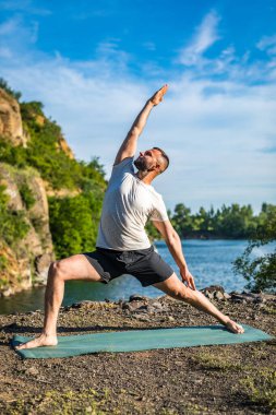 Elleri ve bacakları eşe uzatan bir adam. Sakallı adam taş ocağında ve dağlarda yoga yapıyor..
