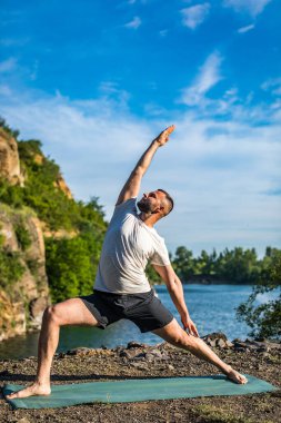 Elleri ve bacakları eşe uzatan bir adam. Sakallı adam taş ocağında ve dağlarda yoga yapıyor..