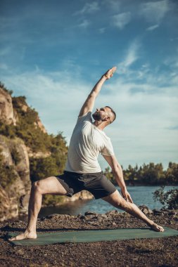 Elleri ve bacakları eşe uzatan bir adam. Sakallı adam taş ocağında ve dağlarda yoga yapıyor..