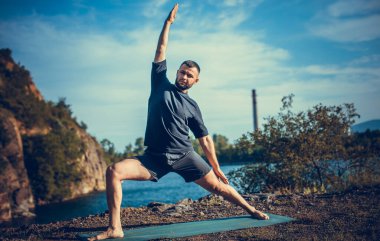 Güneşli bir günde taş ocağı gölünde yoga egzersizi yapan adam. Uluslararası Yoga Günü.