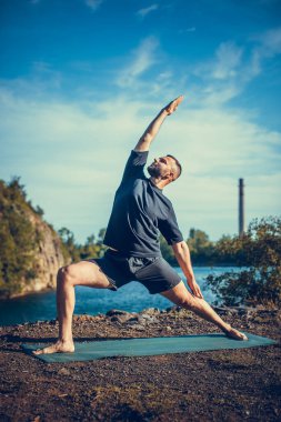 Güneşli bir günde taş ocağı gölünde yoga egzersizi yapan adam. Uluslararası Yoga Günü.