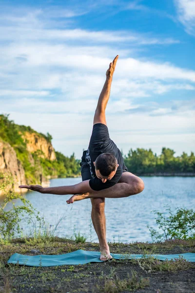 A good looking young bearded man doing yoga on quarry lake backdrop. International Day of Yoga concept.