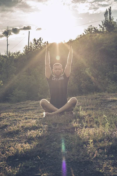 Mükemmel vücut adamının silueti günbatımı arka planında kayanın üzerinde yoga yapıyor. Uluslararası Yoga Günü.
