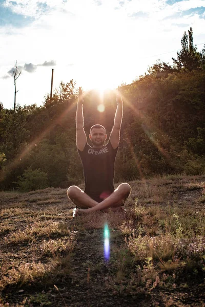 Mükemmel vücut adamının silueti günbatımı arka planında kayanın üzerinde yoga yapıyor. Uluslararası Yoga Günü.