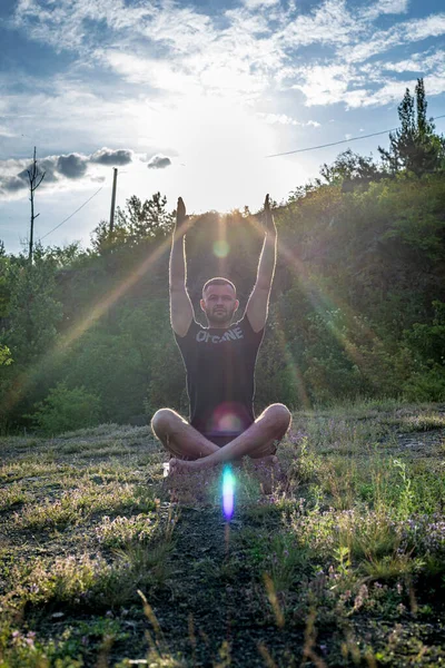 Mükemmel vücut adamının silueti günbatımı arka planında kayanın üzerinde yoga yapıyor. Uluslararası Yoga Günü.