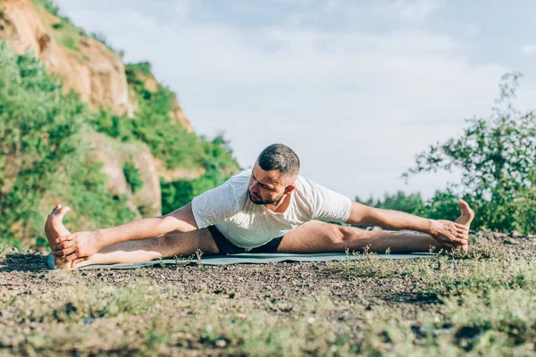 Fitness, insanlar ve sağlıklı yaşam tarzı konsepti. Sakallı adam yoga yapıyor. Minderde poz veriyor. Quarry Lake 'in arka planında. Uluslararası Yoga Günü.