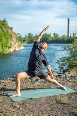 Güneşli bir günde taş ocağı gölünde yoga egzersizi yapan adam. Uluslararası Yoga Günü.
