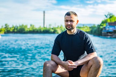 Taş ocağının arka planında kayaların üzerinde oturan sakallı genç adam. Yakışıklı portre..