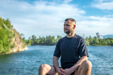Taş ocağının arka planında kayaların üzerinde oturan sakallı genç adam. Yakışıklı portre..
