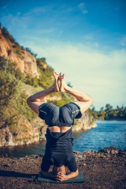 Sakallı, yakışıklı, siyah saçlı, yoga yapan bir adam. Kafasının üstünde duran genç adam Sirshasana 'nın taş ocağı gölünde durduğu pozda..