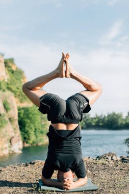 Sakallı, yakışıklı, siyah saçlı, yoga yapan bir adam. Kafasının üstünde duran genç adam Sirshasana 'nın taş ocağı gölünde durduğu pozda..