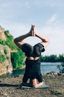 Sakallı, yakışıklı, siyah saçlı, yoga yapan bir adam. Kafasının üstünde duran genç adam Sirshasana 'nın taş ocağı gölünde durduğu pozda..
