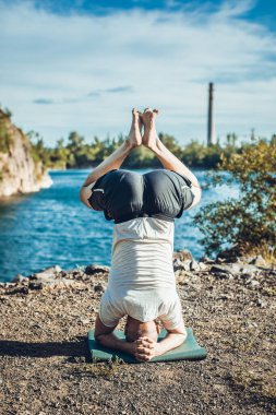 Sakallı, yakışıklı, siyah saçlı, yoga yapan bir adam. Kafasının üstünde duran genç adam Sirshasana 'nın taş ocağı gölünde durduğu pozda..