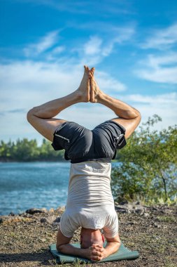 Güçlü sağlıklı atletik adam sabah antrenmanı yapıyor taş ocağı gölünde yoga yapıyor, baş aşağı duruyor. Rahatlama ve meditasyon, sağlıklı yaşam tarzı konsepti. Uluslararası Yoga Günü.