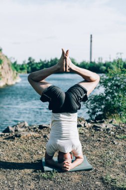 Güçlü sağlıklı atletik adam sabah antrenmanı yapıyor taş ocağı gölünde yoga yapıyor, baş aşağı duruyor. Rahatlama ve meditasyon, sağlıklı yaşam tarzı konsepti. Uluslararası Yoga Günü.