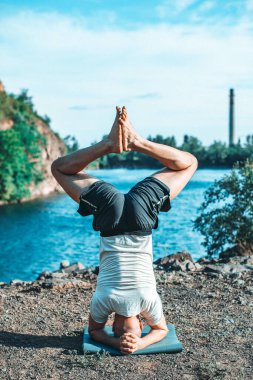 Güçlü sağlıklı atletik adam sabah antrenmanı yapıyor taş ocağı gölünde yoga yapıyor, baş aşağı duruyor. Rahatlama ve meditasyon, sağlıklı yaşam tarzı konsepti. Uluslararası Yoga Günü.