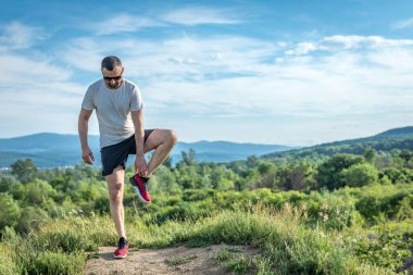 Genç sakallı gezgin ayakları arkasında günbatımı dağlarıyla tek başına duruyor. Yaşam tarzı seyahat kavramı.