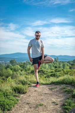 Genç sakallı gezgin ayakları arkasında günbatımı dağlarıyla tek başına duruyor. Yaşam tarzı seyahat kavramı.