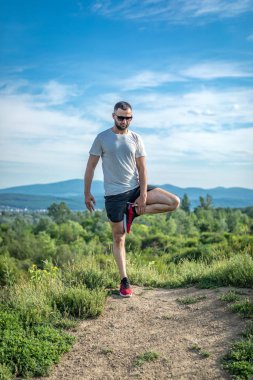 Genç sakallı gezgin ayakları arkasında günbatımı dağlarıyla tek başına duruyor. Yaşam tarzı seyahat kavramı.