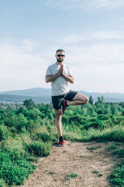Genç sakallı gezgin ayakları arkasında günbatımı dağlarıyla tek başına duruyor. Yaşam tarzı seyahat kavramı.