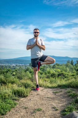 Genç sakallı gezgin ayakları arkasında günbatımı dağlarıyla tek başına duruyor. Yaşam tarzı seyahat kavramı.