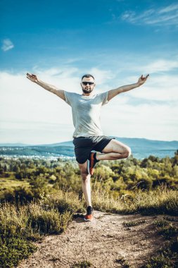 Genç sakallı gezgin ayakları arkasında günbatımı dağlarıyla tek başına duruyor. Yaşam tarzı seyahat kavramı.