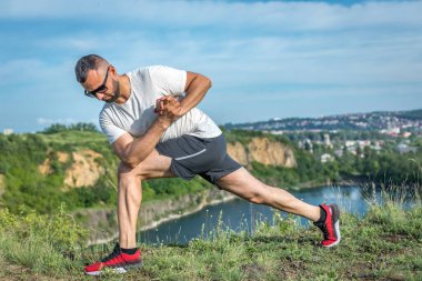 Profesyonel fitness eğitmeni. Sakallı sporcu antrenman yapıyor, taş ocağı gölünde geriniyor. Açık hava spor konsepti.