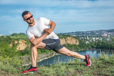 Profesyonel fitness eğitmeni. Sakallı sporcu antrenman yapıyor, taş ocağı gölünde geriniyor. Açık hava spor konsepti.