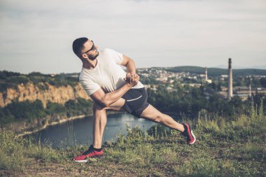 Profesyonel fitness eğitmeni. Sakallı sporcu antrenman yapıyor, taş ocağı gölünde geriniyor. Açık hava spor konsepti.