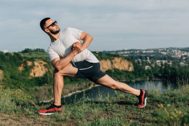 Profesyonel fitness eğitmeni. Sakallı sporcu antrenman yapıyor, taş ocağı gölünde geriniyor. Açık hava spor konsepti.