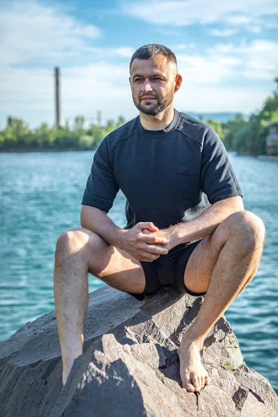 Taş ocağının arka planında kayaların üzerinde oturan sakallı genç adam. Yakışıklı portre..