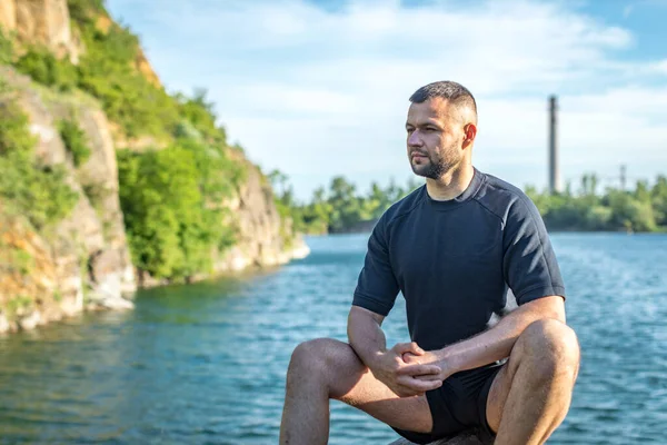 Taş ocağının arka planında kayaların üzerinde oturan sakallı genç adam. Yakışıklı portre..